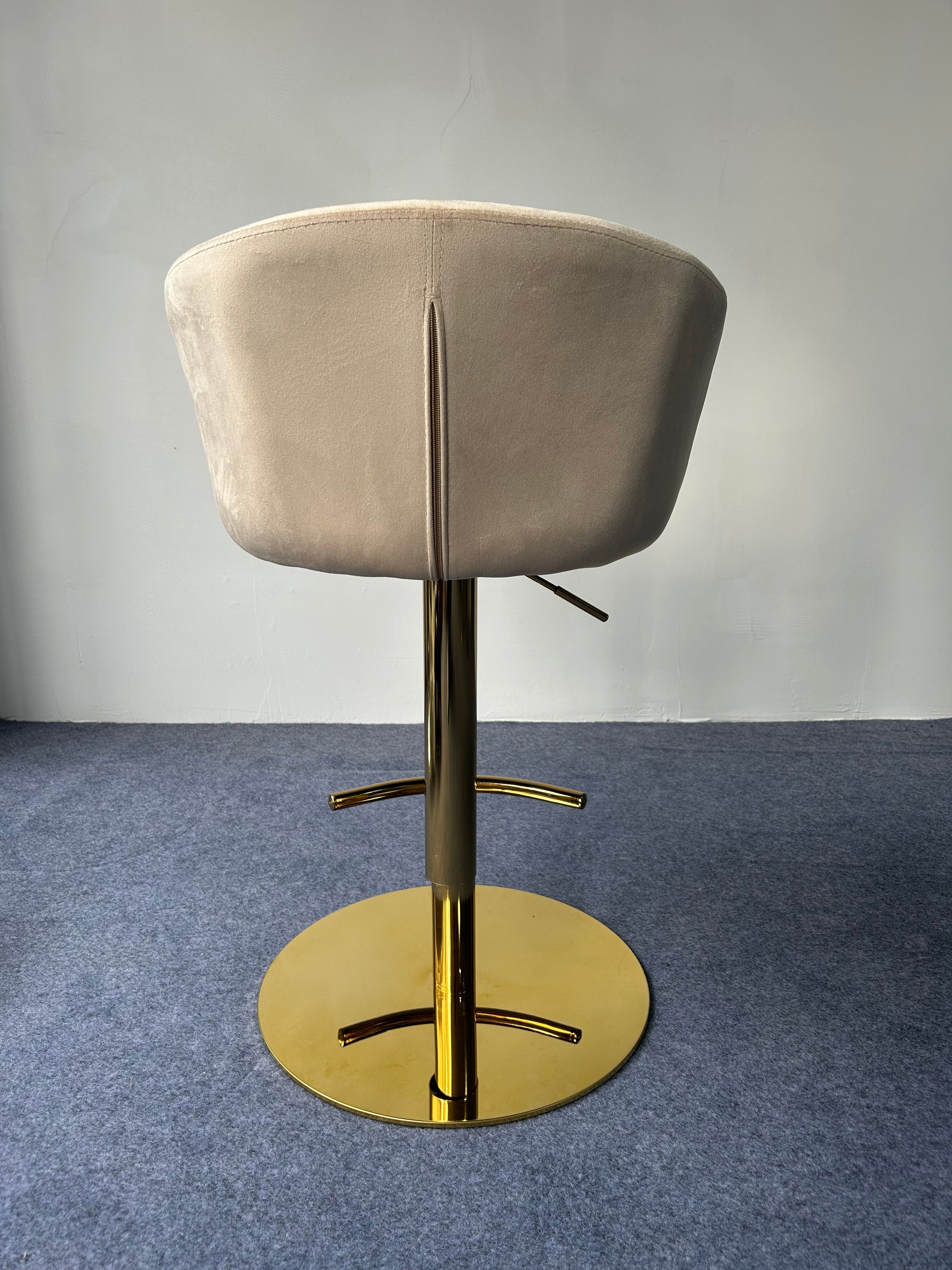 Modern Golden Barstool with a soft beige seat and golden base, viewed from the back on a blue carpet.